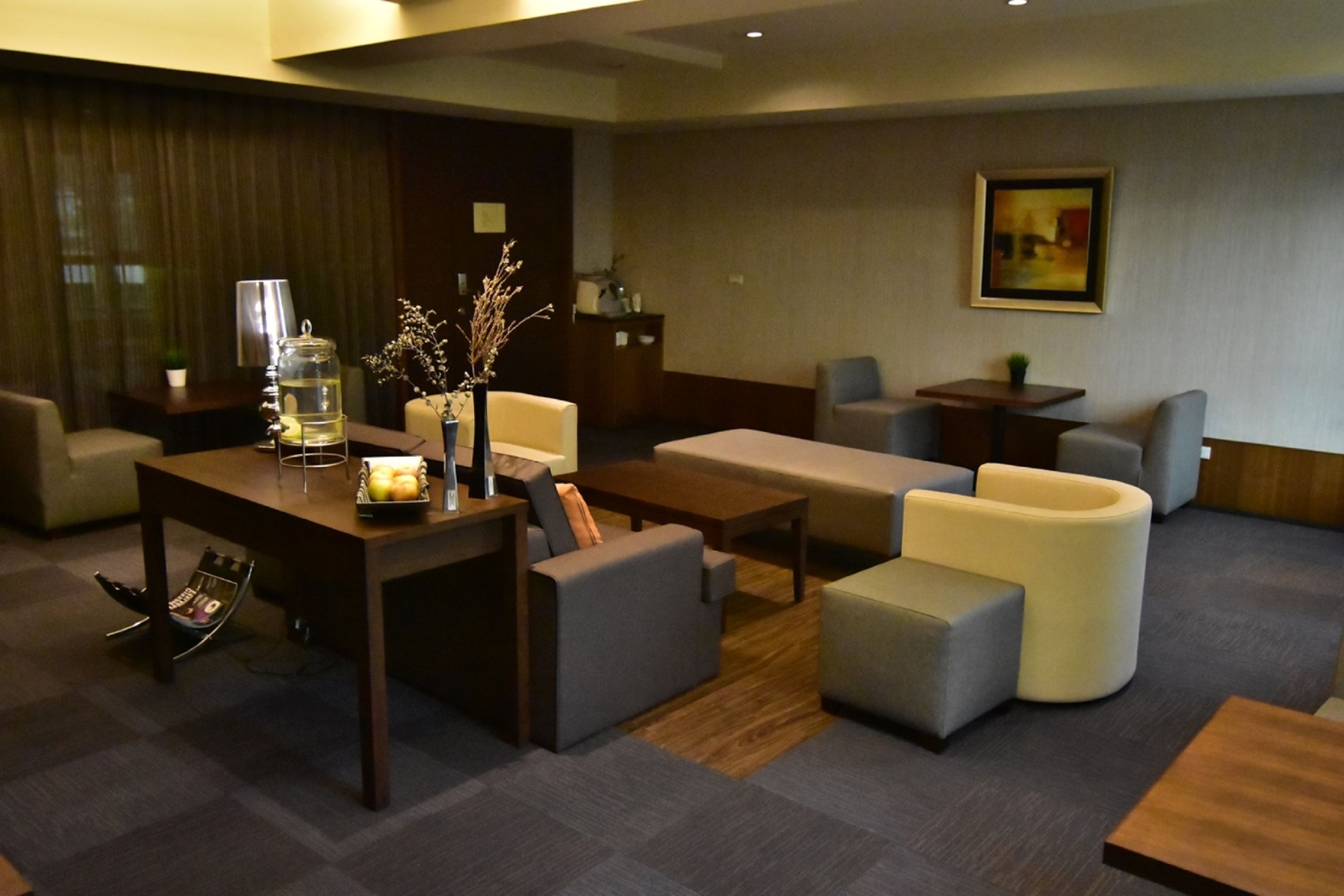A modern hotel lobby with a wooden reception desk, comfortable seating areas, and a decorative vase with branches.