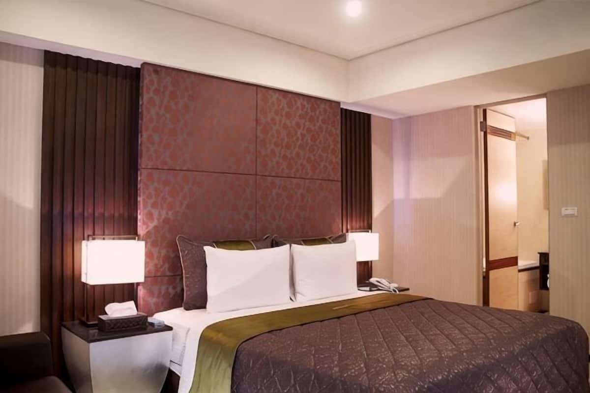 A hotel room with a bed, two bedside lamps, a telephone, a nightstand, and a door.