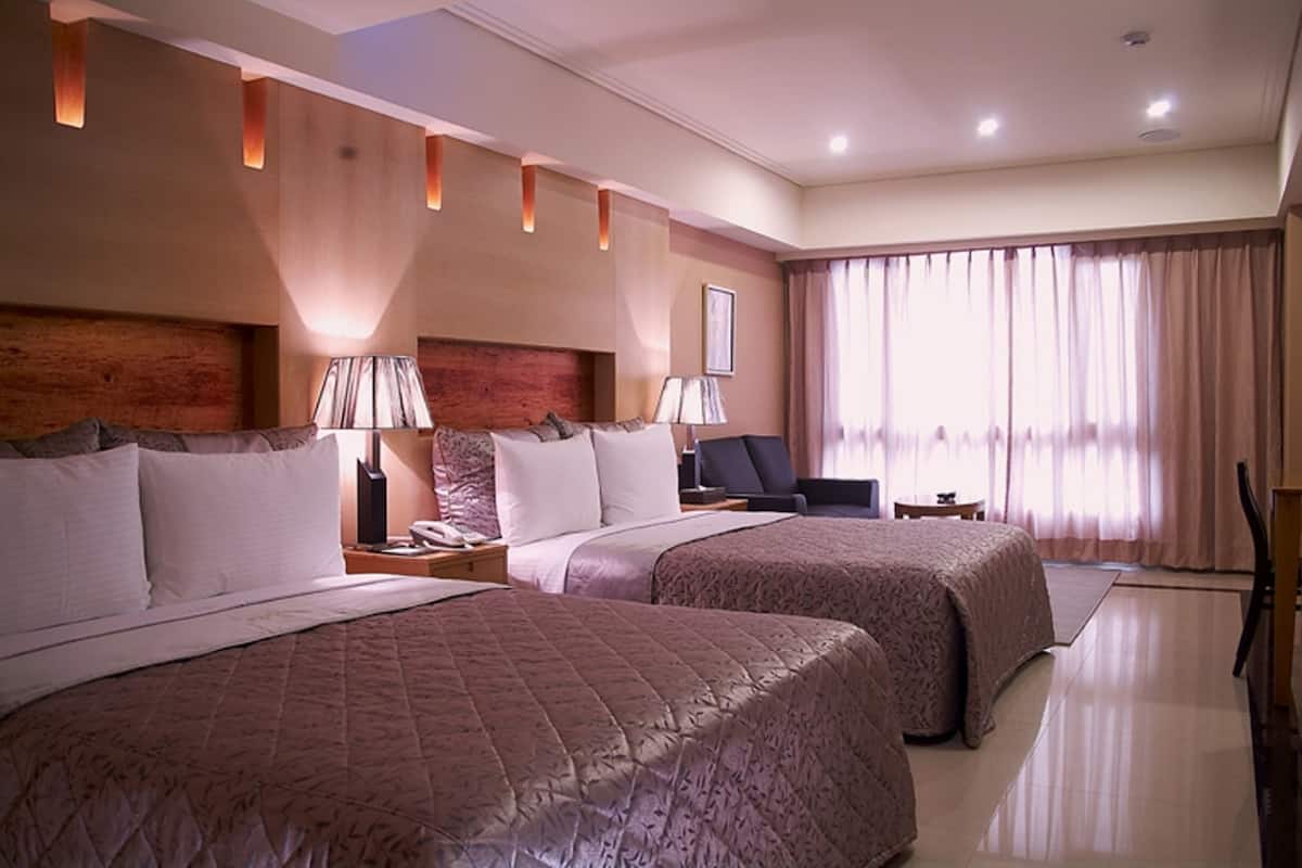 A hotel room with two queen beds, a desk, a chair, and a large window with curtains.