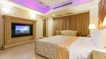 A hotel room with a large bed, a television mounted on a brick wall, a sofa, and a lamp on a bedside table.