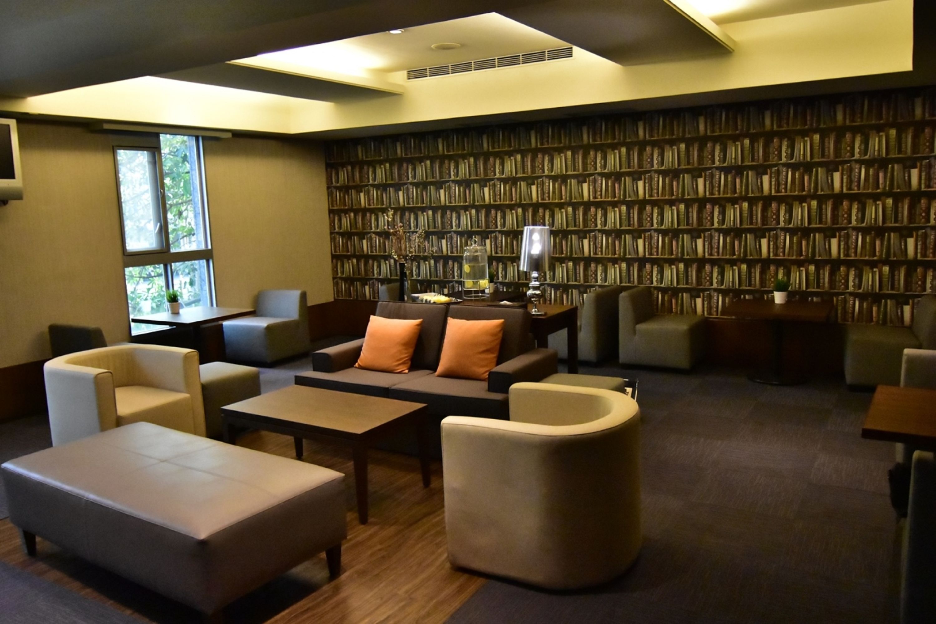 A modern library with a large bookshelf, comfortable seating, and a large window.