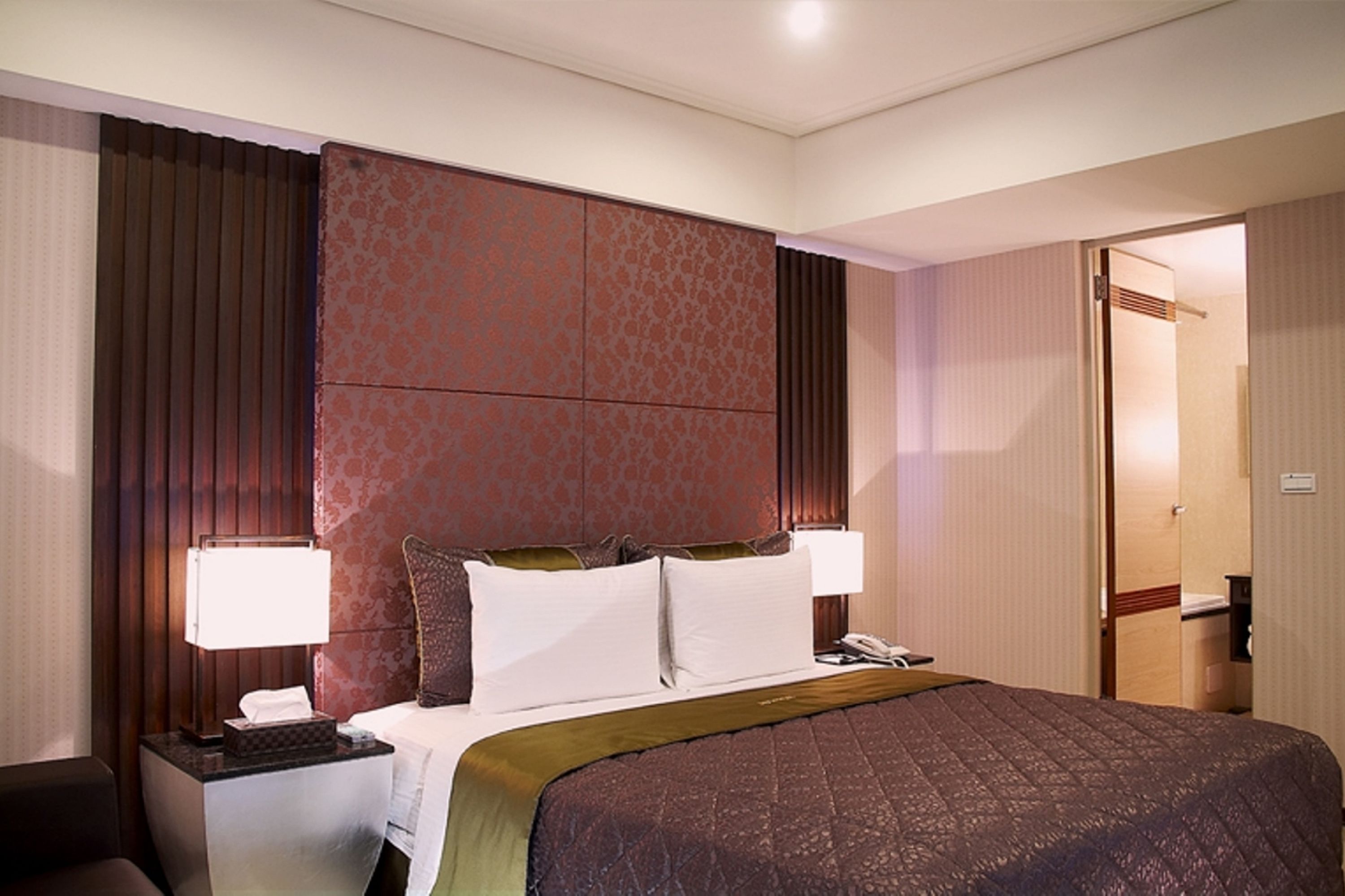 Una habitación de hotel con una cama grande, dos mesitas de noche, un teléfono y una puerta al baño.