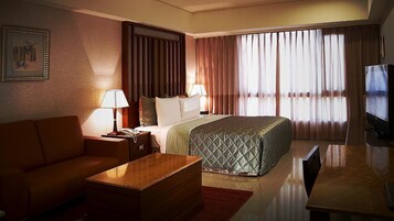 Una habitación de hotel con cama, sofá, escritorio, televisor y cortinas.