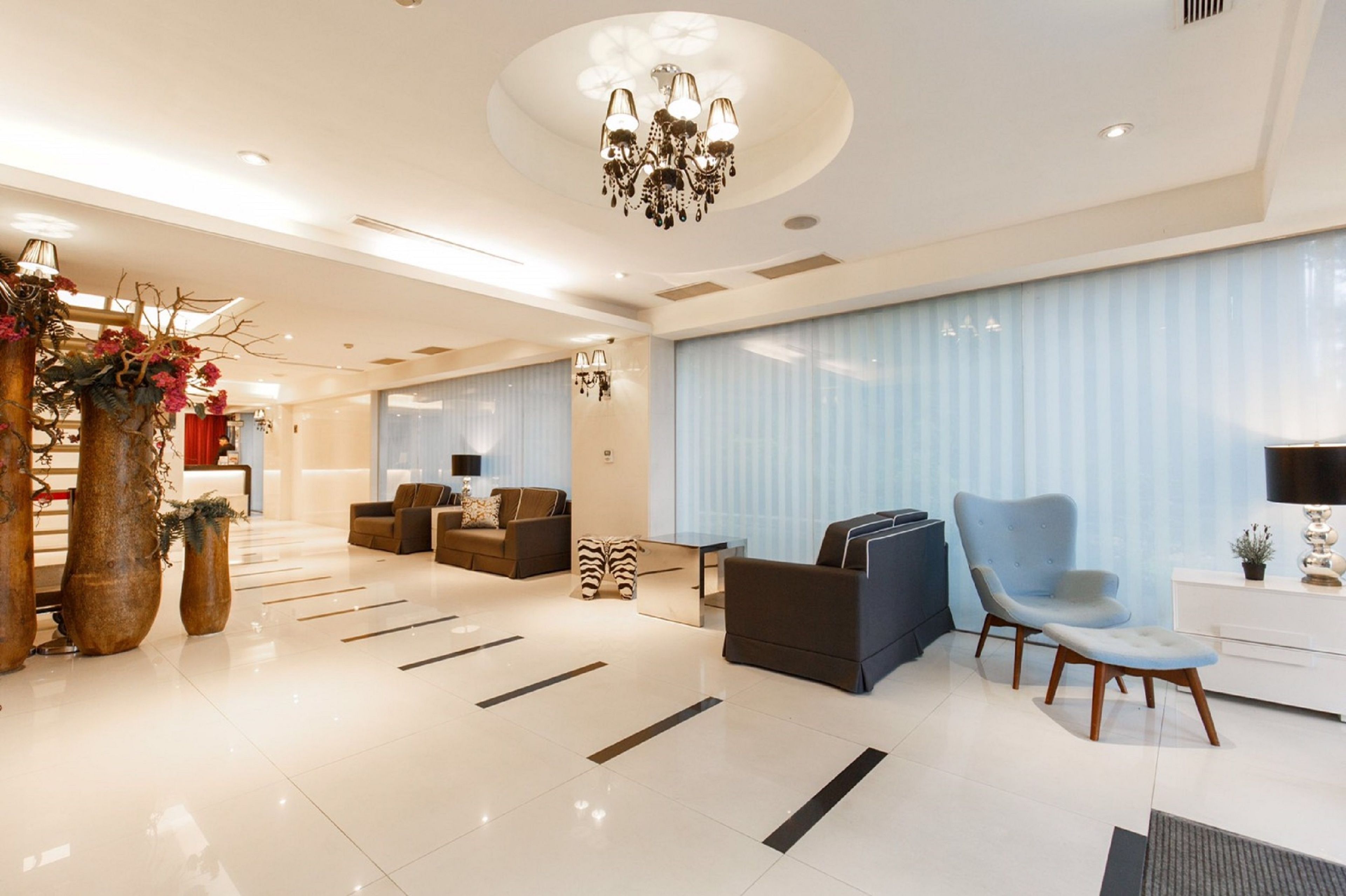 A modern hotel lobby with a chandelier, seating area, and large windows.