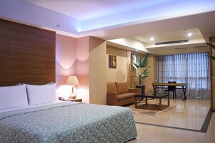 Una habitación de hotel con una cama, un sofá, una mesa de centro, un escritorio y una planta.