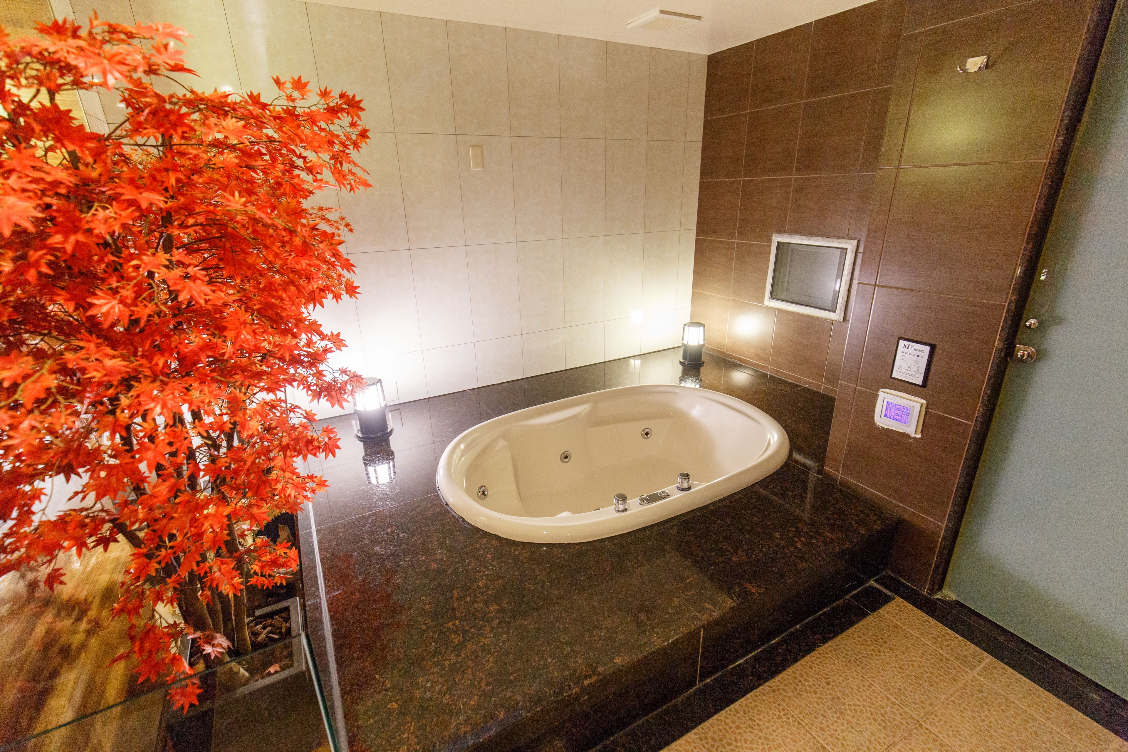 A modern bathroom with a large bathtub, a glass shower enclosure, and a decorative red maple tree.