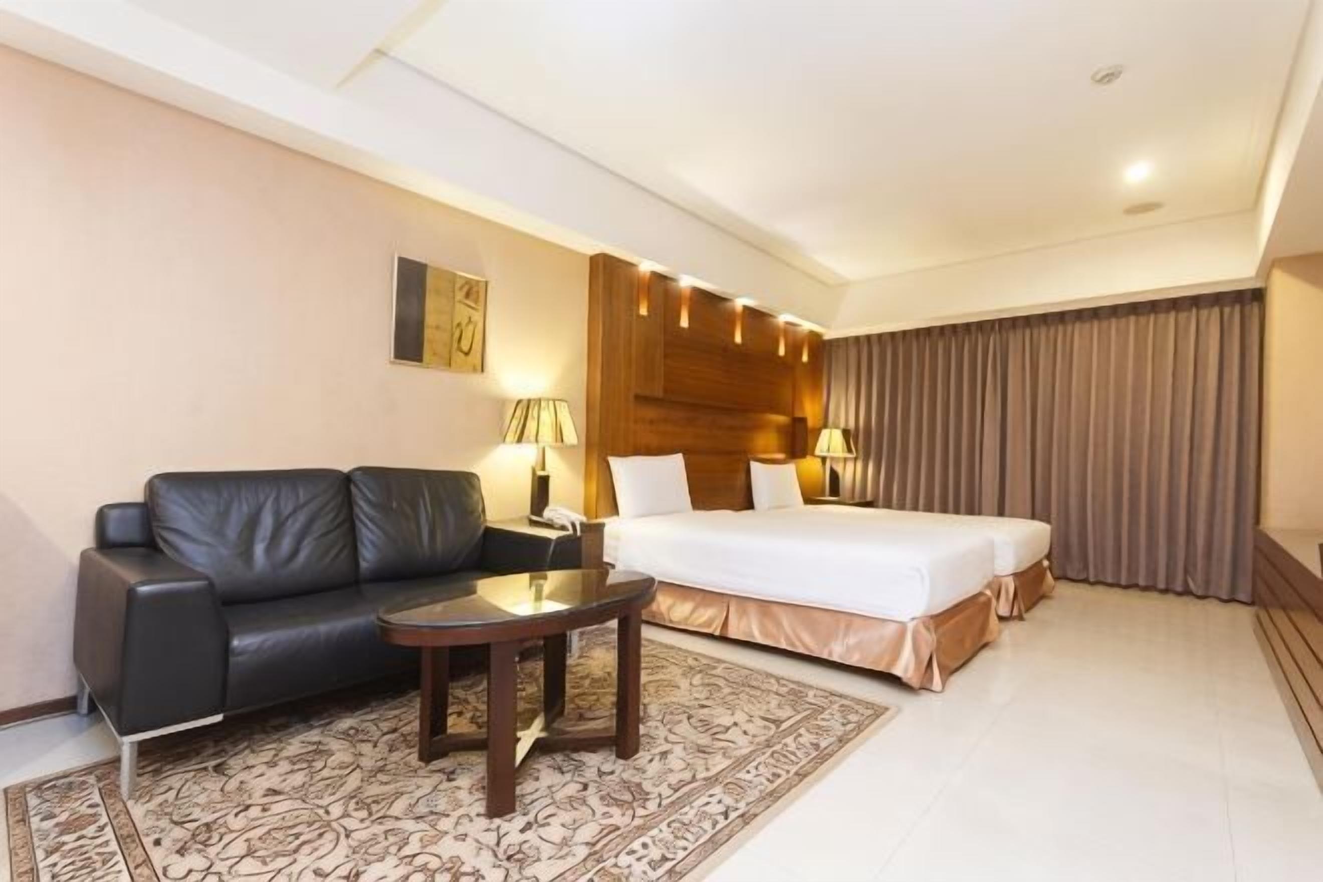 A hotel room with a bed, a sofa, a small table, and a lamp.
