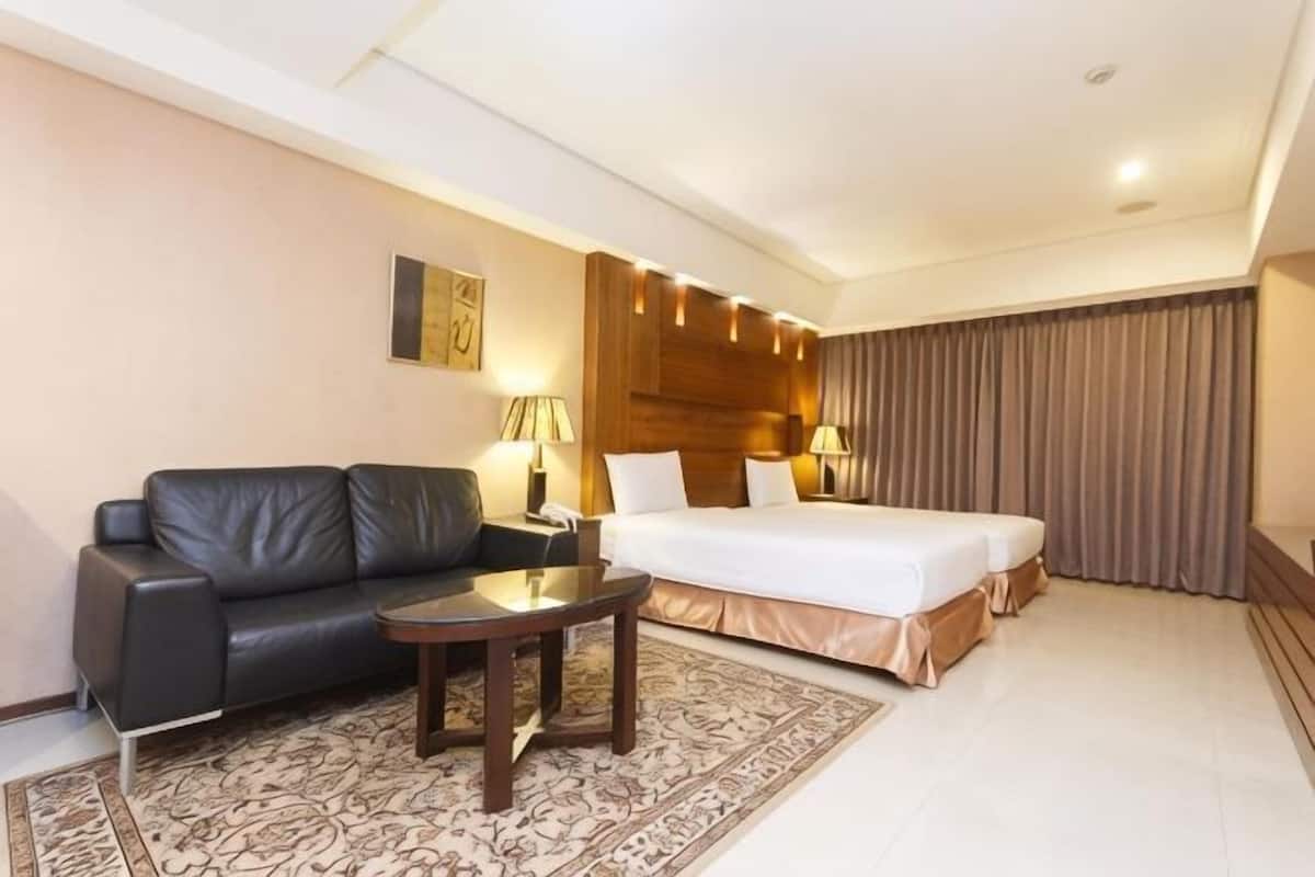 A hotel room with a bed, a sofa, a small table, and a lamp.