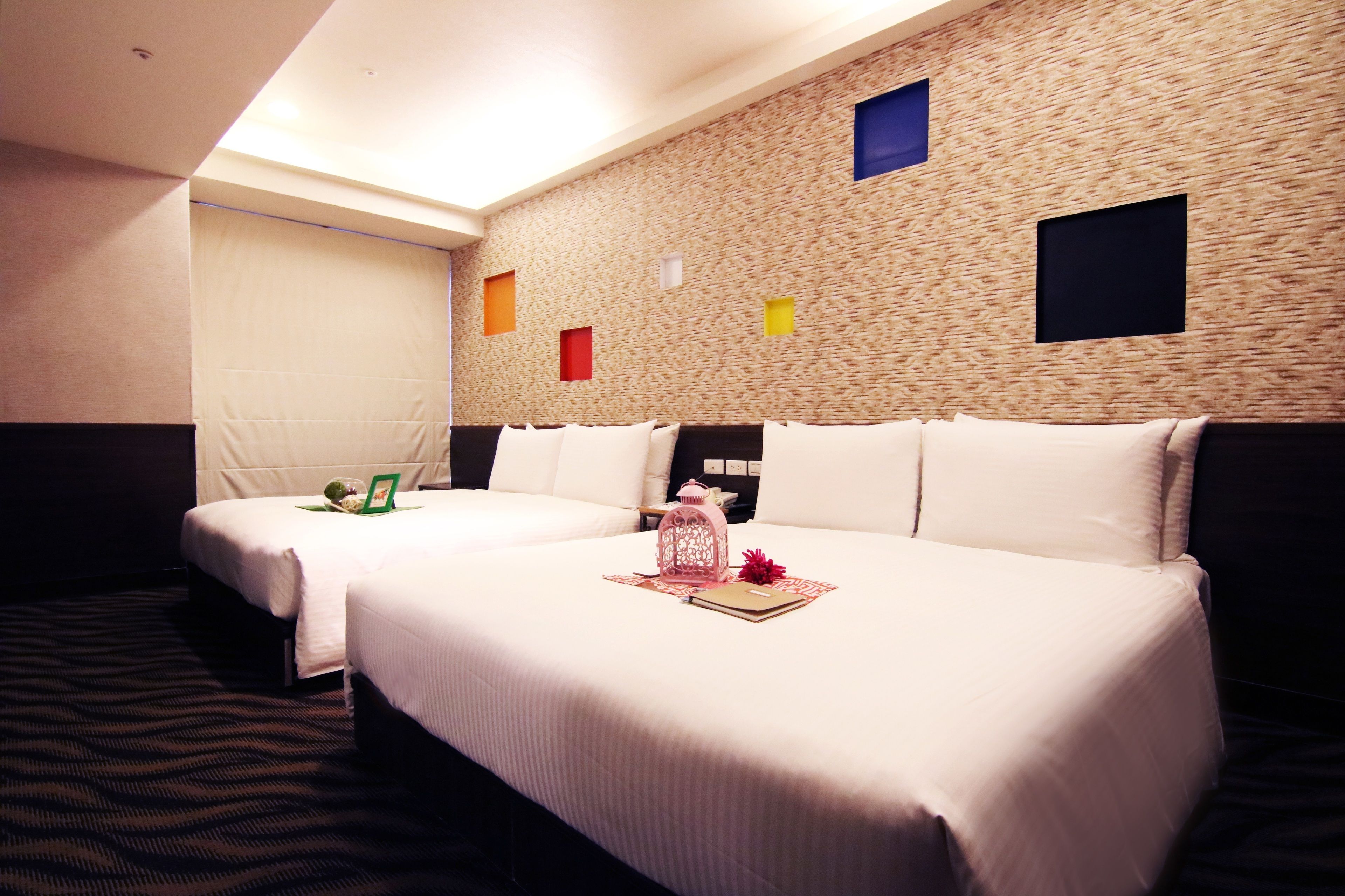 A hotel room with two beds, a patterned carpet, and a textured wall with colored squares.