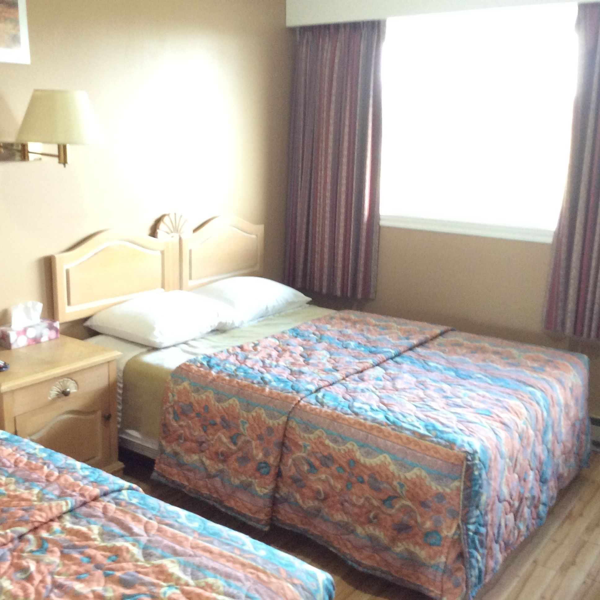 A hotel room with two beds, a nightstand, a lamp, and a window with curtains.