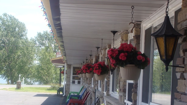 A covered porch with hanging flower baskets and a row of colorful chairs. - Lion Motel (South Stormont)