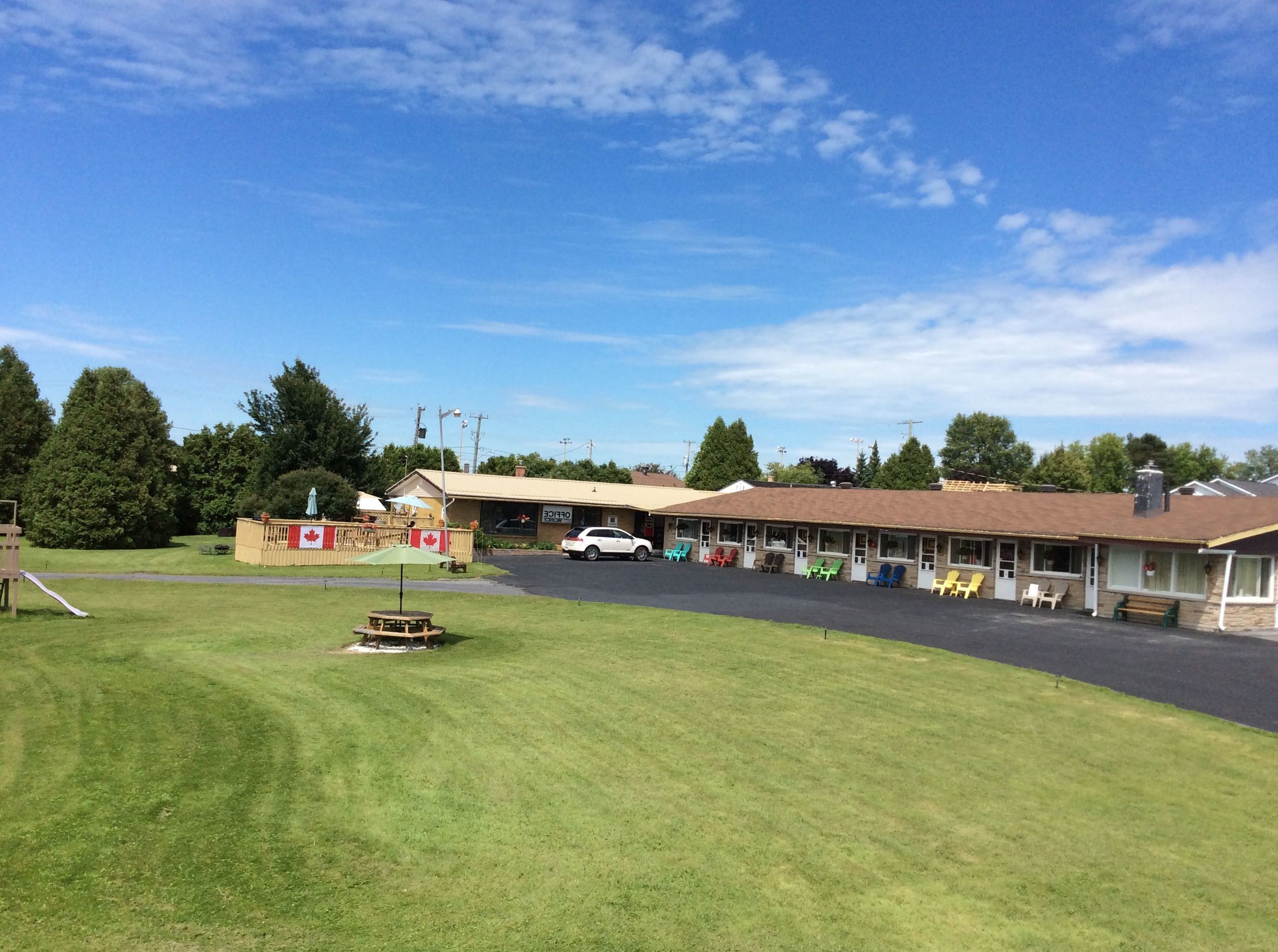 A motel with a covered parking area, outdoor seating, and a flag.