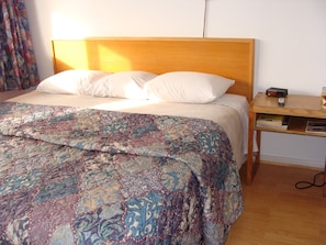 A bed with a patterned quilt, a wooden headboard, and a nightstand with a remote control and books.
