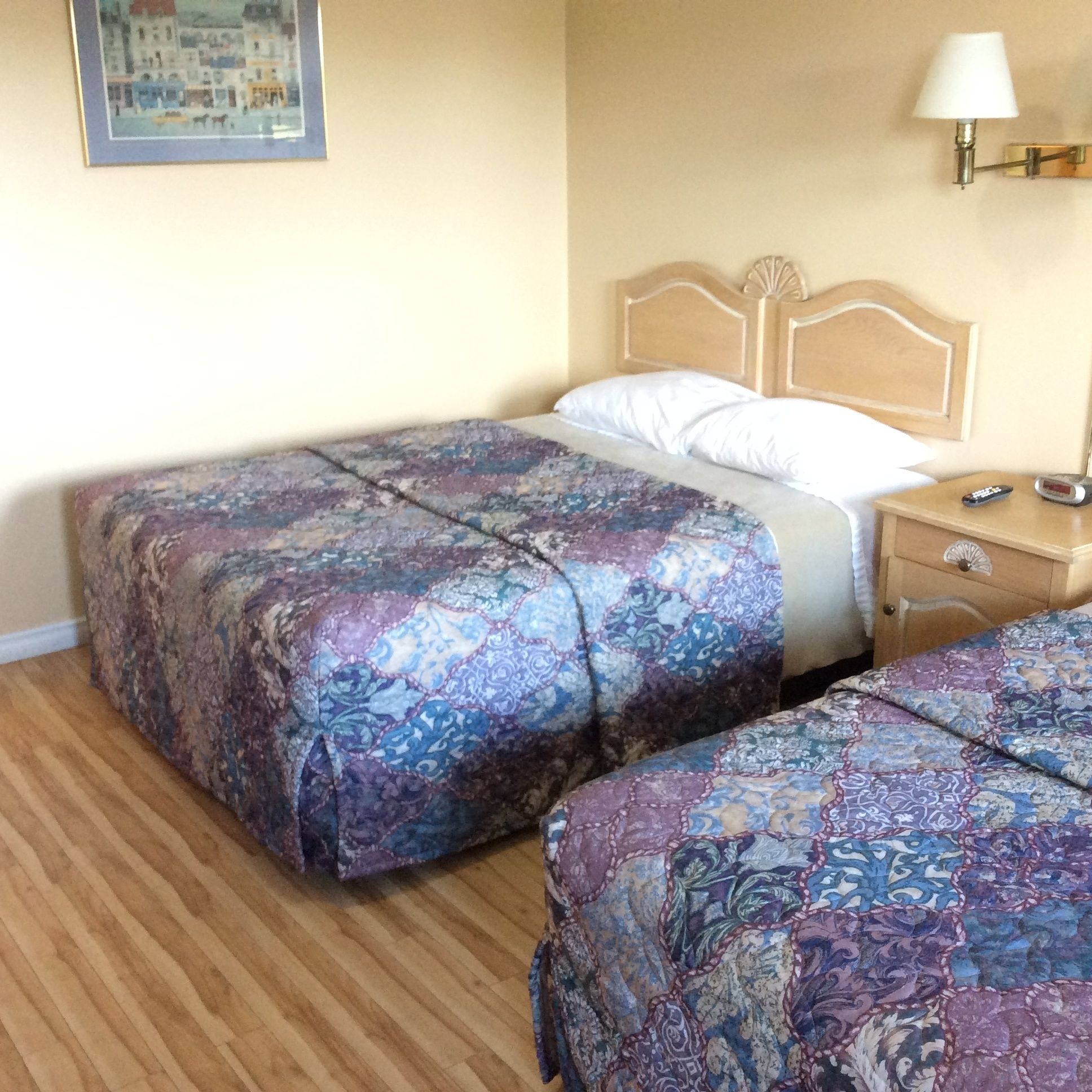 Ein Hotelzimmer mit zwei Betten, Holz-Kopfteilen, einem Nachttisch mit Lampe und einem gerahmten Bild an der Wand.