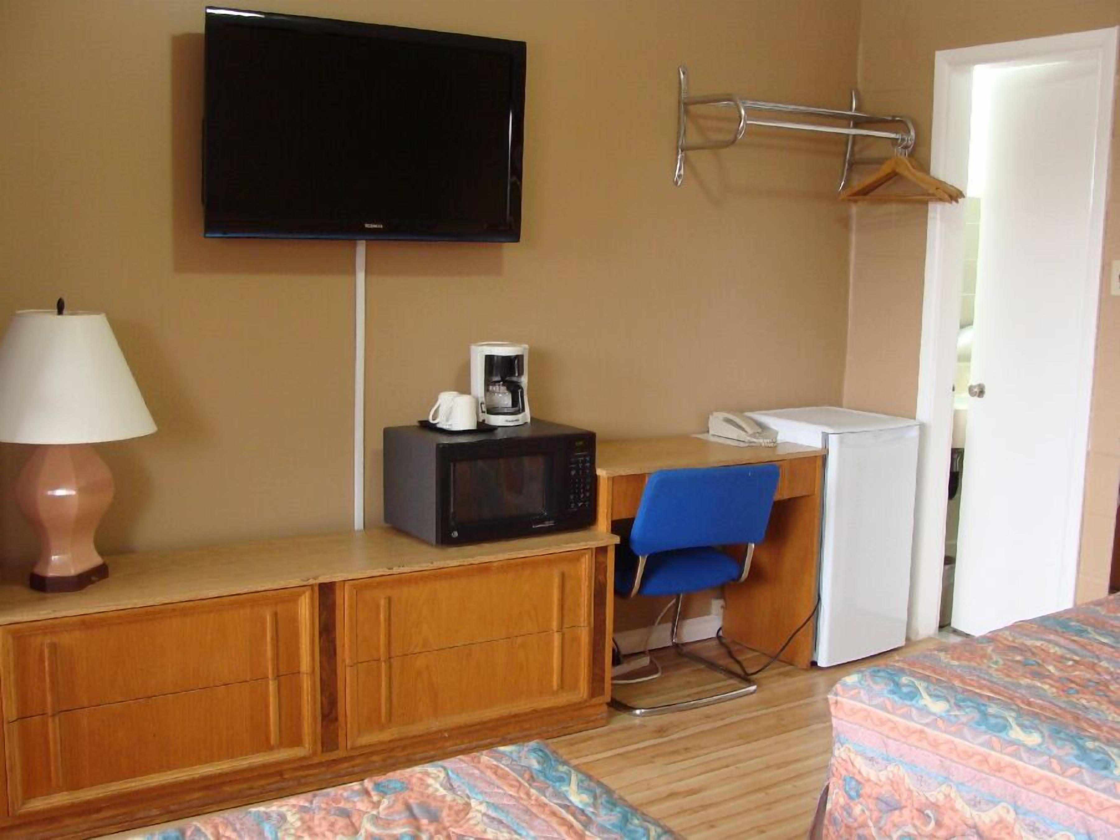 A hotel room with a bed, a desk with a microwave, a TV, a lamp, and a chair.