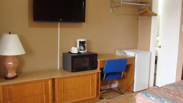 A hotel room with a bed, a desk with a microwave, a TV, a lamp, and a chair.