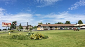A motel with a large sign, a parking lot, and a grassy area with flowers. - Lion Motel (South Stormont)