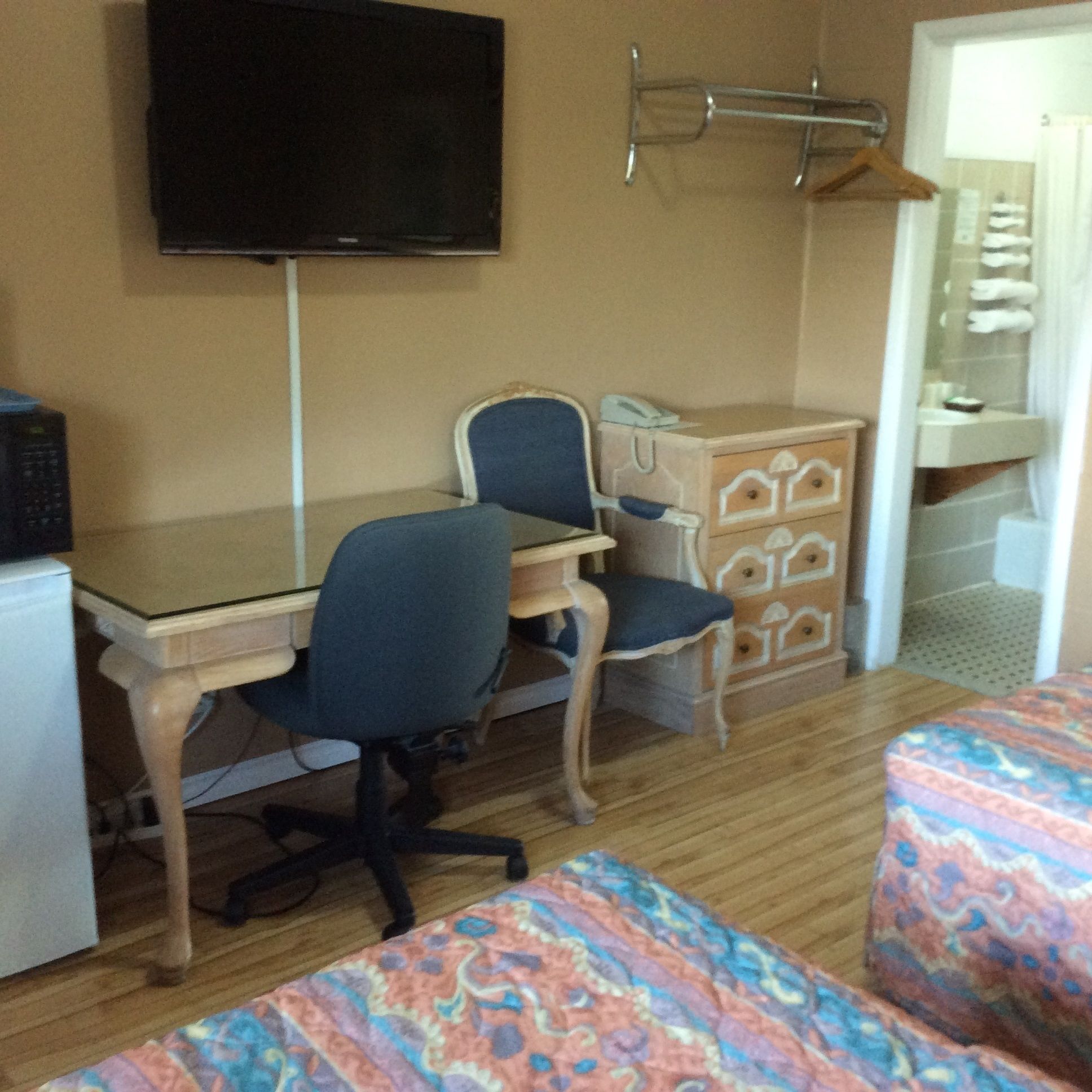 A room with a desk, two chairs, a television, a wardrobe, and a bed with patterned bedding.