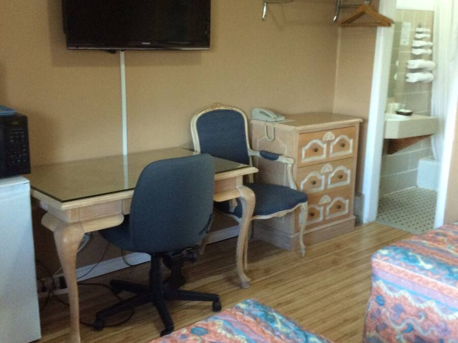 A room with a desk, two chairs, a television, a wardrobe, and a bed with patterned bedding.