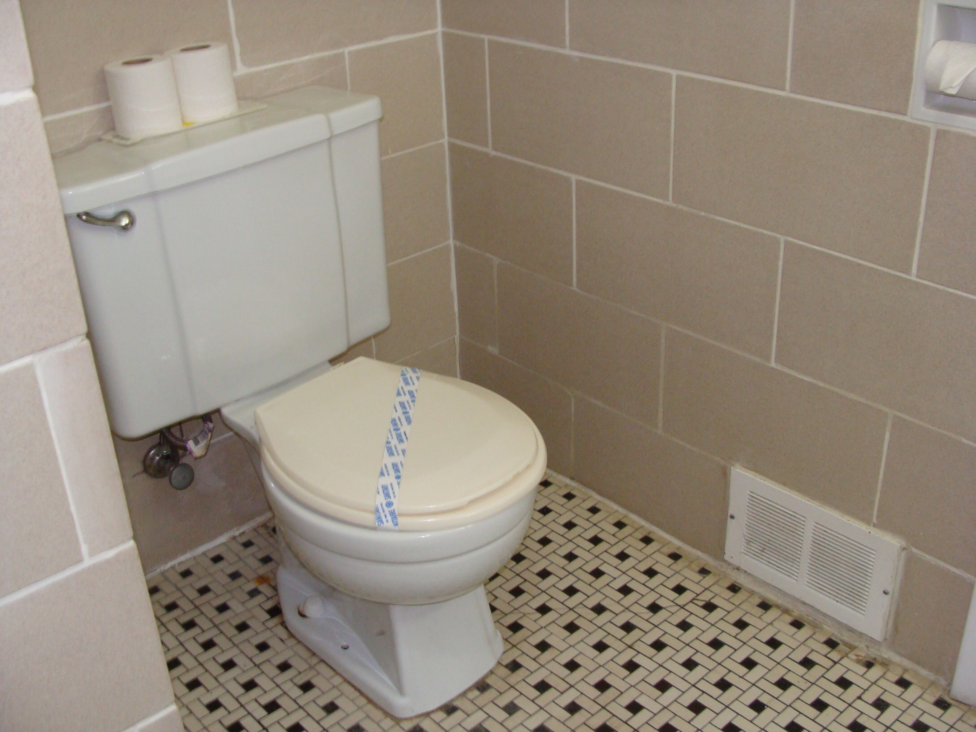 Un baño con inodoro, dispensador de papel higiénico en la pared y suelo con un diseño de baldosas blanco y negro.