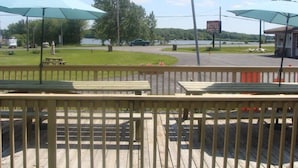 A motel with a deck, picnic tables, and umbrellas overlooking a lake. - Lion Motel (South Stormont)