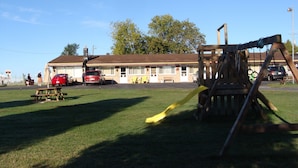 A motel with a parking lot, a swing set, and a picnic table. - Lion Motel (South Stormont)