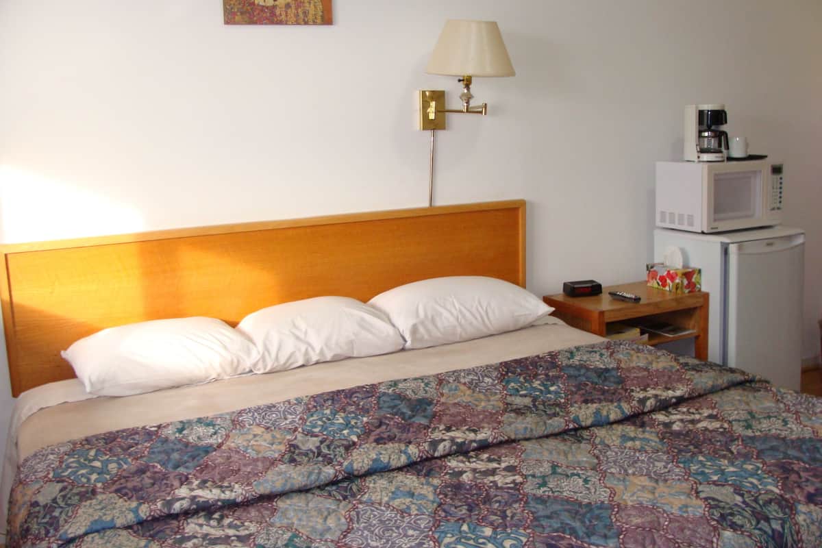 Ein Hotelzimmer mit einem hölzernen Kopfteil, einer gemusterten Bettdecke, einer Nachttischlampe, einem Nachttisch mit Fernbedienung, einer Mikrowelle und einem Kühlschrank.