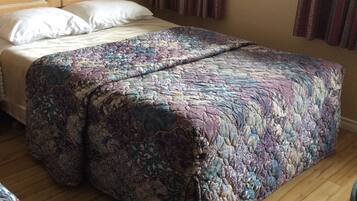 Un dormitorio con cabecera de madera, colcha estampada y ventana con cortinas.