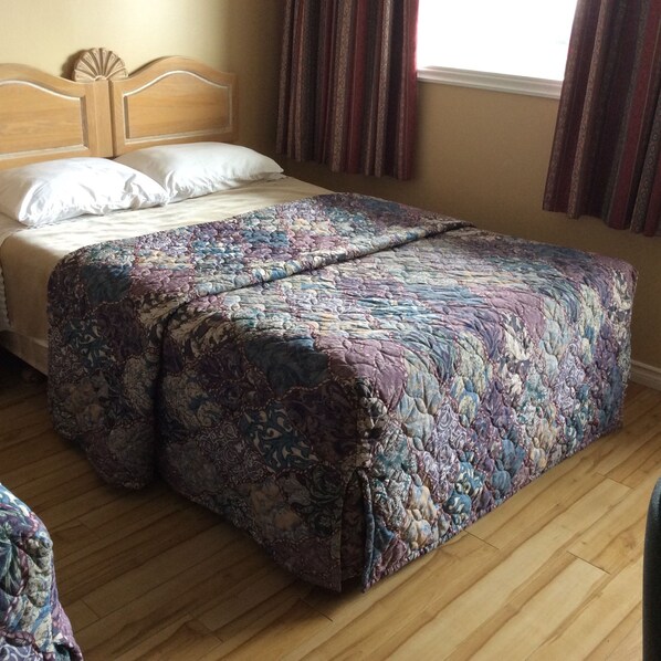 A bedroom with a wooden headboard, a floral bedspread, and a window with curtains.