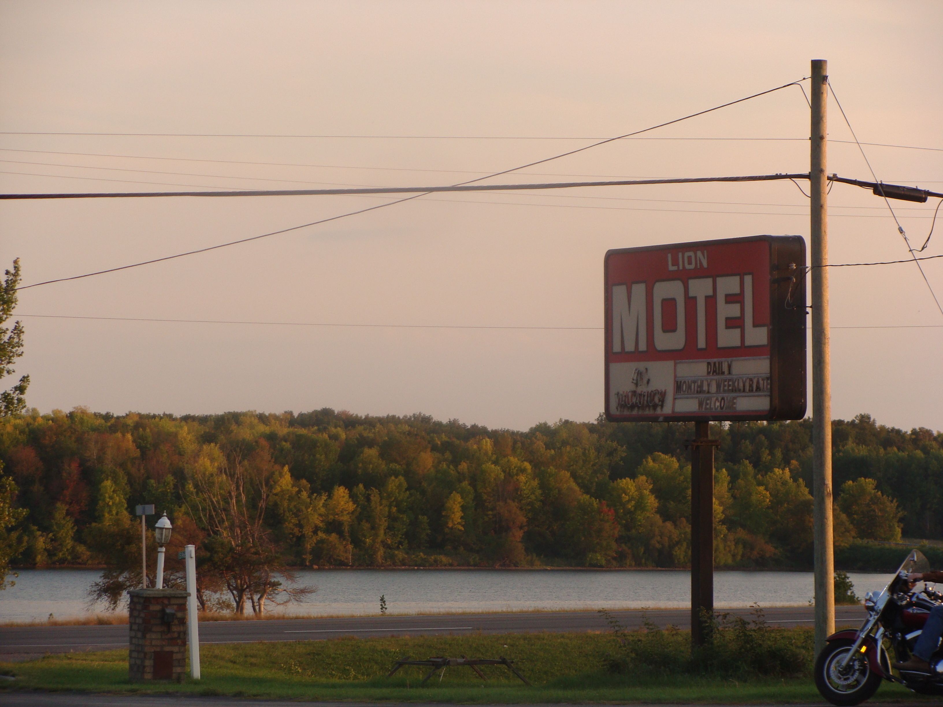 A motel sign with a view of a lake and trees in the background.