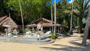 Un resort con estructuras de techo de paja, una zona de piscina y palmeras.