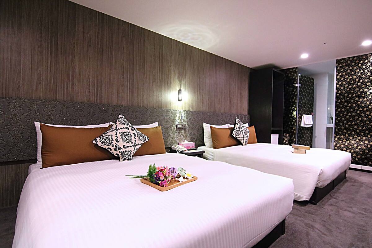 A hotel room with two beds, each with a wooden headboard, a nightstand, and a tray with flowers.