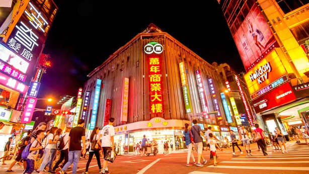 A brightly lit building with large signage and a crowd of people in front. - Hotel 6 - Wannien (Taipei)