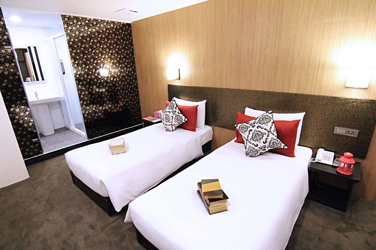 A hotel room with two beds, a bedside table with a lamp, a mirror, and a bathroom visible through an open door.