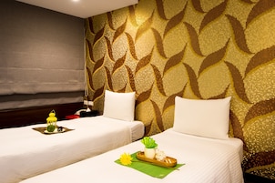 Habitación de hotel con dos camas, un papel tapiz estampado y una pequeña mesa con un farol y una bandeja con objetos.