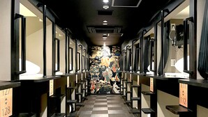 A hotel corridor with checkered flooring, individual rooms on either side, and a central wall with a decorative mural.