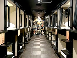 Egy hotel folyosó, kockás mintájú padlóval, melynek mindkét oldalán külön-külön szobák találhatók, és a folyosó közepén egy díszes falfestmény látható.