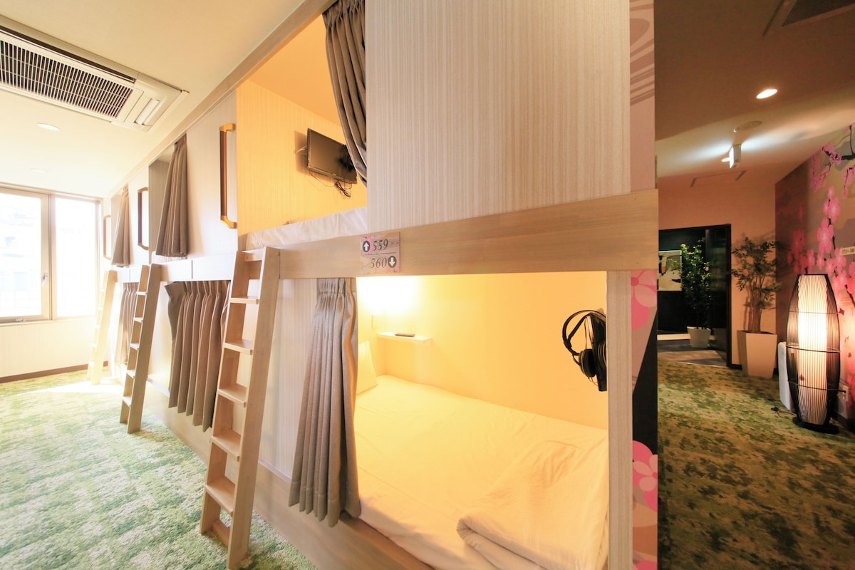 Une chambre avec un lit superposé, une échelle, une table de chevet et un téléviseur fixé au mur.