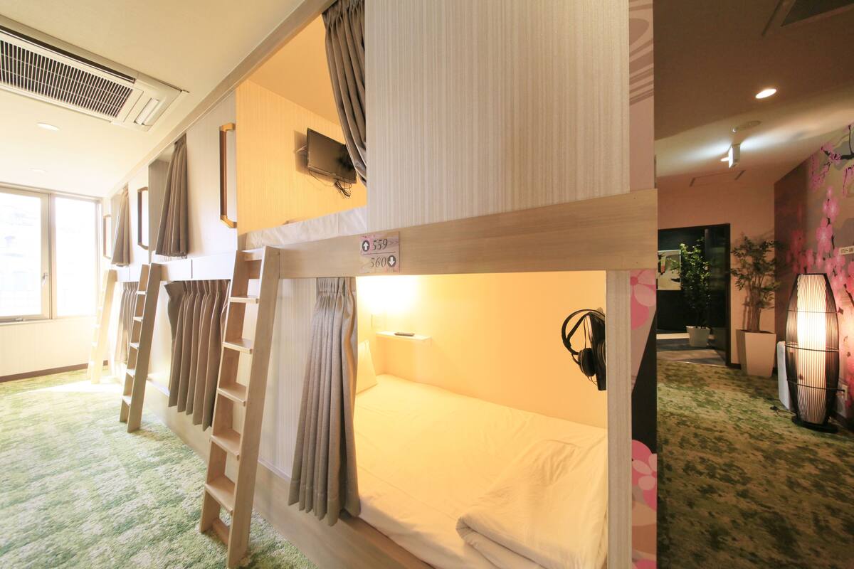 A bunk bed room with a ladder, a bedside table, and a wall-mounted TV.