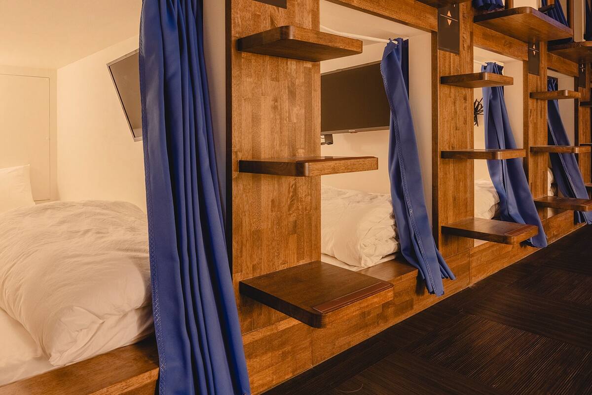 A hotel room with a bed, a TV mounted on the wall, and a wooden shelf unit with curtains.