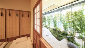 A traditional Japanese-style room with tatami flooring, shoji screens, and a view of a landscaped garden through a glass window. - Ueno Station Hostel Oriental 1 - Caters to Men (Tokyo)