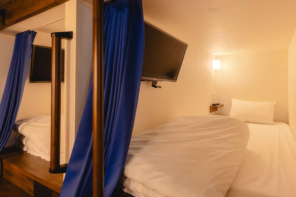A bedroom with a bed, a TV mounted on the wall, and a bedside table with a lamp.