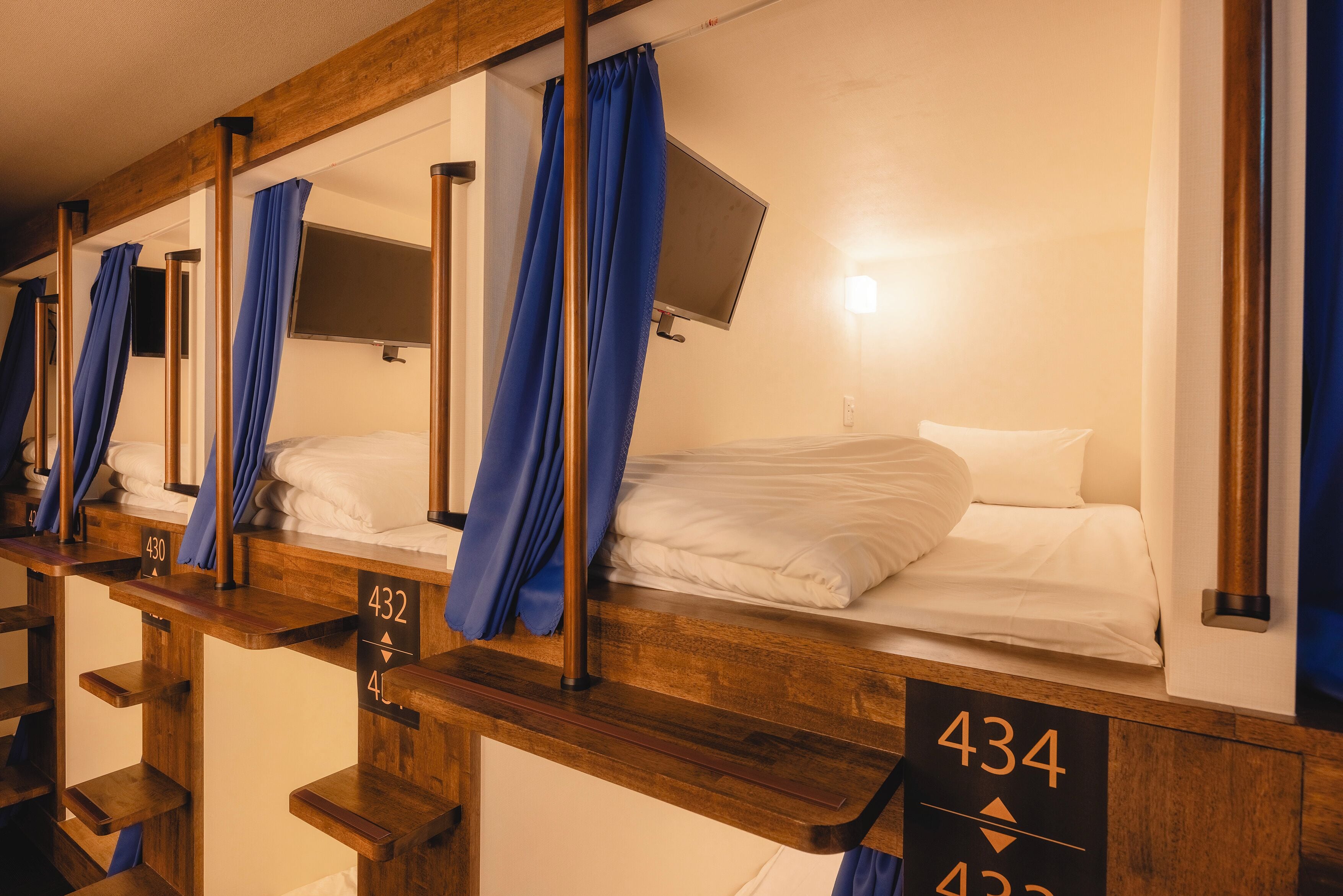 A row of wooden bunk beds with blue curtains, each bed marked with a number.