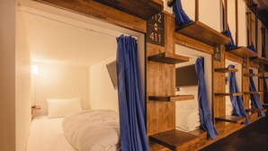 A hotel room with a bed, a wooden shelf unit with numbers, and a curtain. - UENO STATION HOSTEL ORIENTAL 2 - Cater to Men (Tokyo)