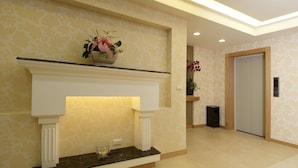 A hallway with a fireplace, a potted plant, a trash bin, and a door. - Hotel Color (New Taipei City)