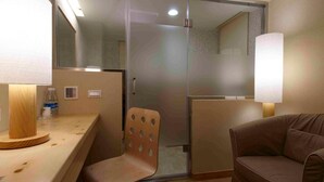 A hotel room with a sliding glass door leading to a bathroom, a wooden side table, a brown leather chair, and a wall-mounted lamp. - Hotel Color (New Taipei City)