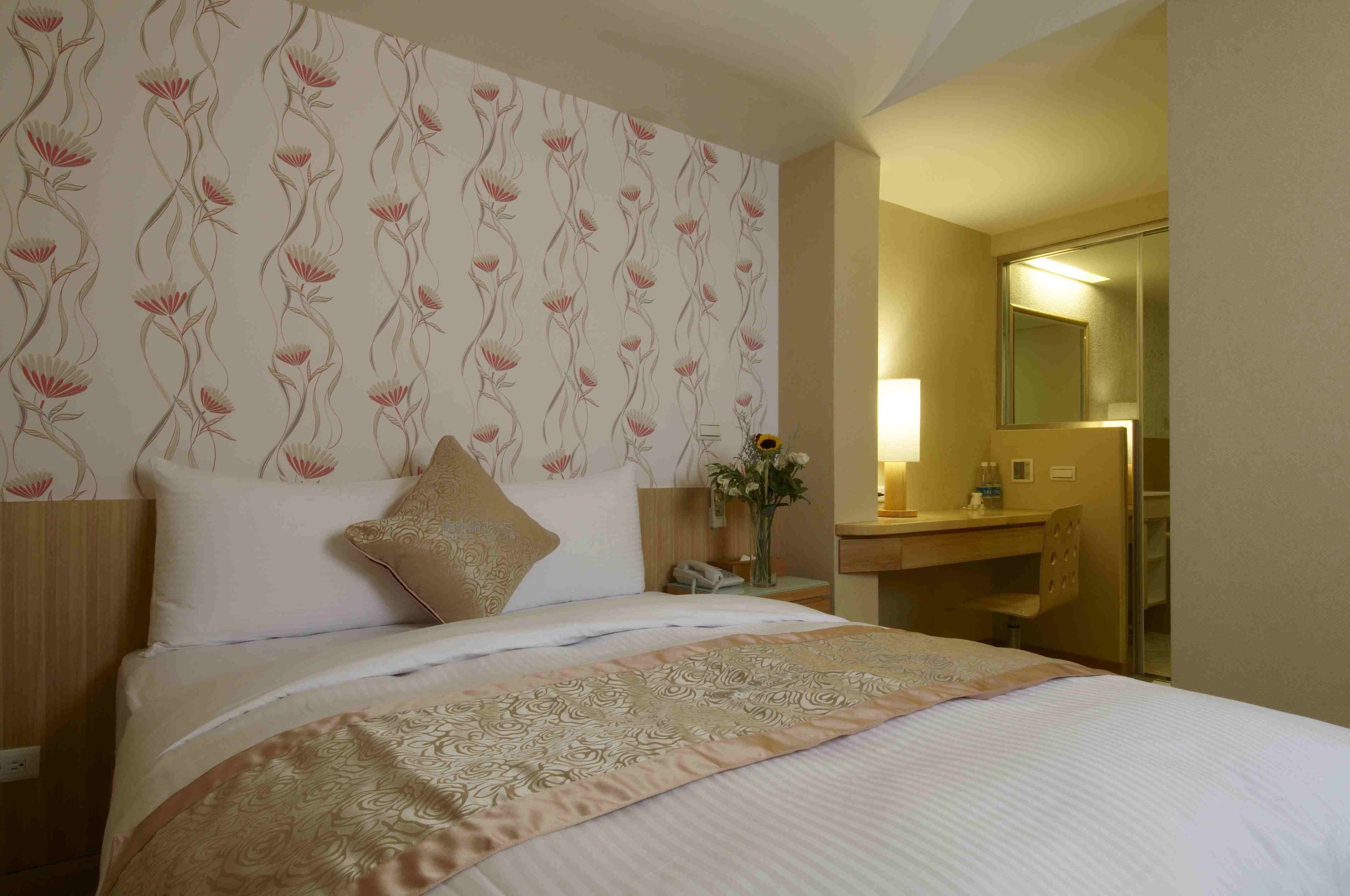 A hotel room with a large bed, a bedside table with a lamp, a mirror, and a bathroom visible through an open door.