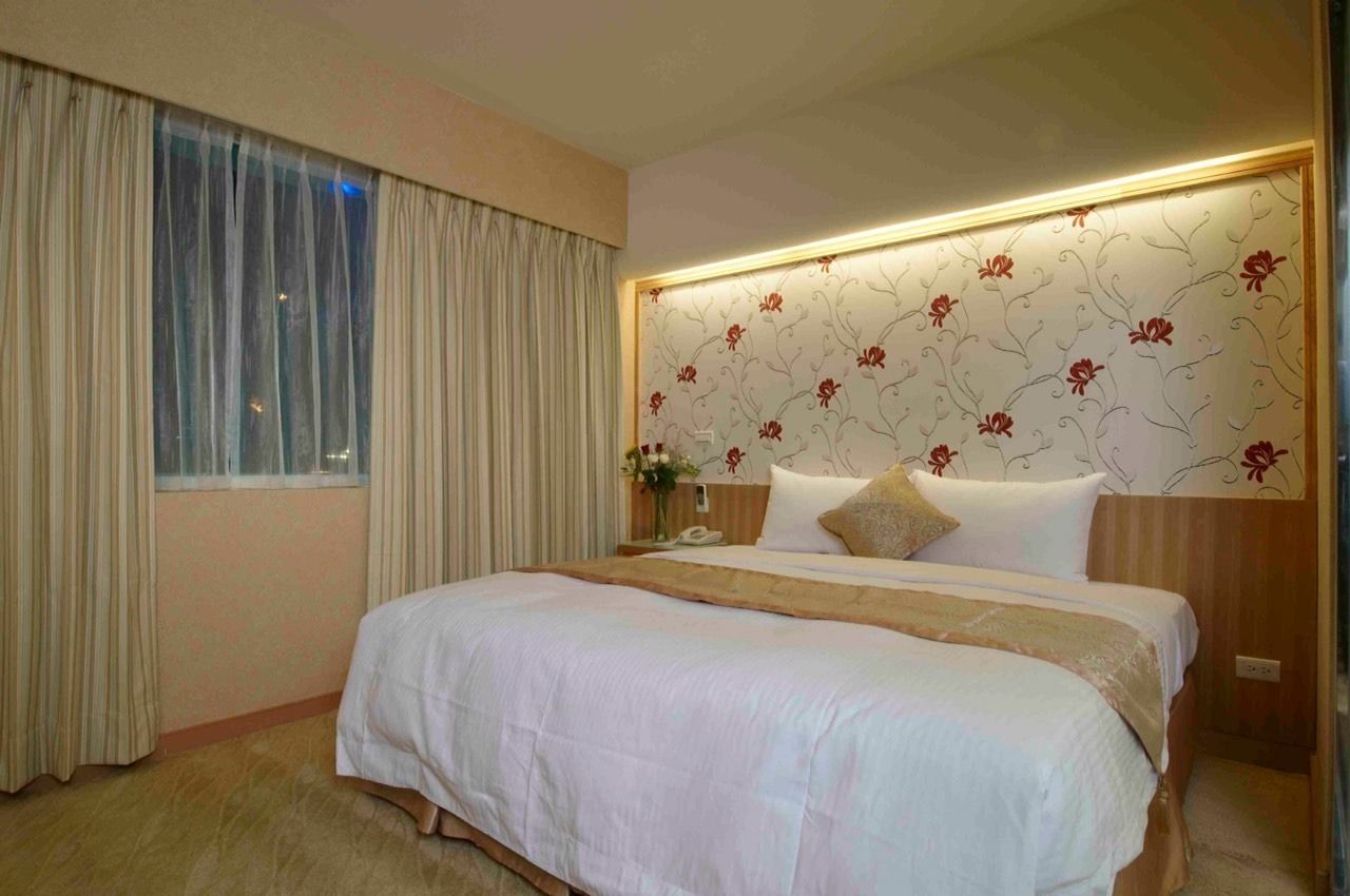 Une chambre d’hôtel avec un grand lit, une table de chevet avec une lampe et une fenêtre avec des rideaux.
