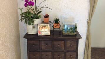 Een houten dressoir met verschillende vakken, een potplant, een ingelijste foto, een klein terrarium en een decoratief object erboven.