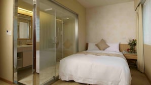A hotel room with a bed, a nightstand, a mirror, a bathroom with a glass shower enclosure, and a wall-mounted air conditioner. - Hotel Color (New Taipei City)